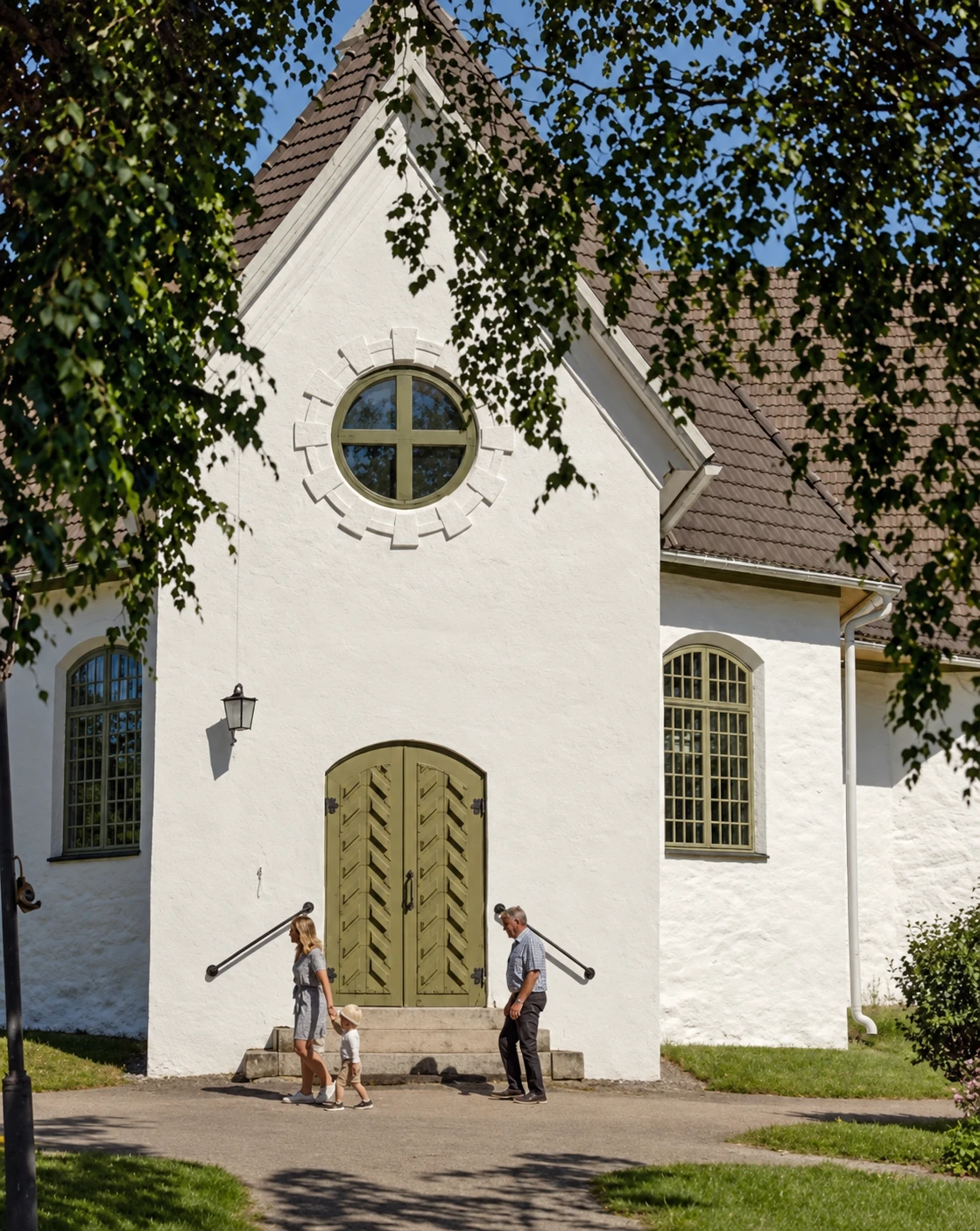 Närpes kyrkas vita fasad och gröna dörr, inramade av sommargrönska.